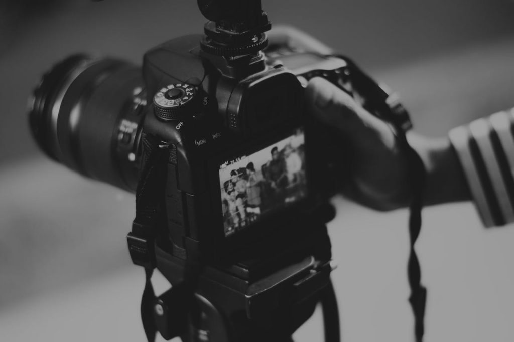 grayscale-photography-of-person-holding-black-dslr-camera-403495 Black and white image of a DSLR camera capturing people in focus, showcasing photography professionalism.