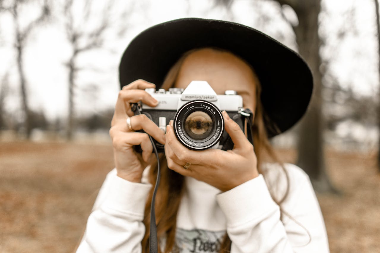 Stylish woman in black hat holding a vintage camera outdoors during fall.