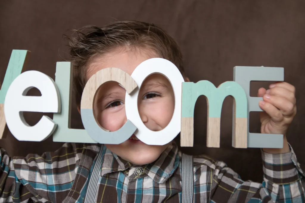 Portrait d’un enfant souriant tenant les lettres du mot “Welcome”, photo réalisée en studio dans les Hautes-Pyrénées, symbole d’accueil et de bonne humeur