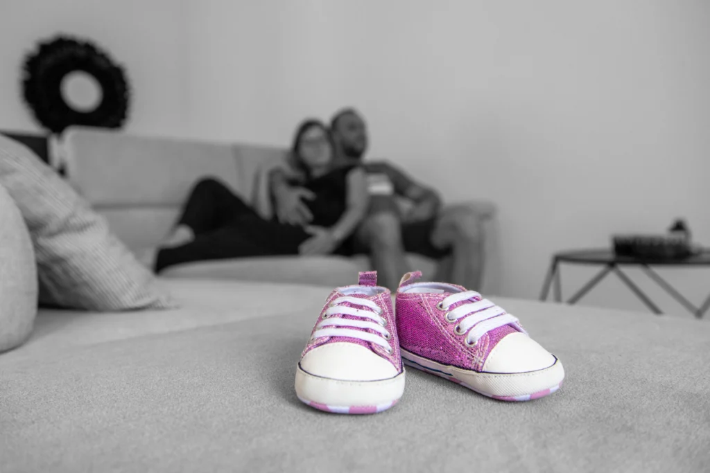 Photo artistique de grossesse avec des petites chaussures de bébé et un couple en arrière-plan