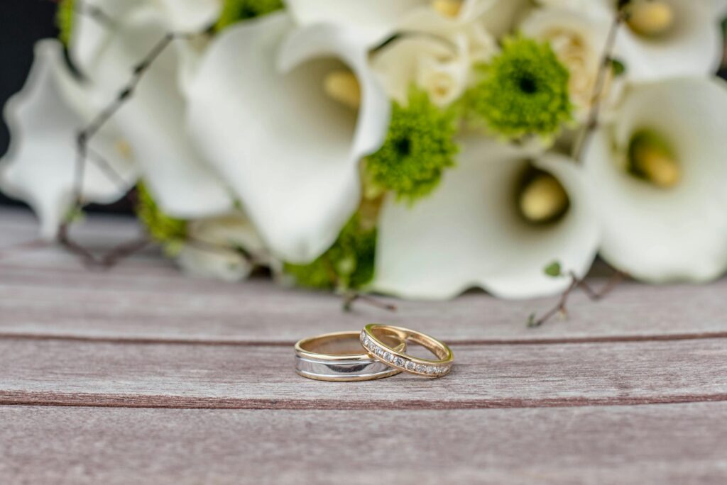 pexels photo 4639481 4639481 Close-up of wedding rings on wooden surface with white and green floral arrangement.