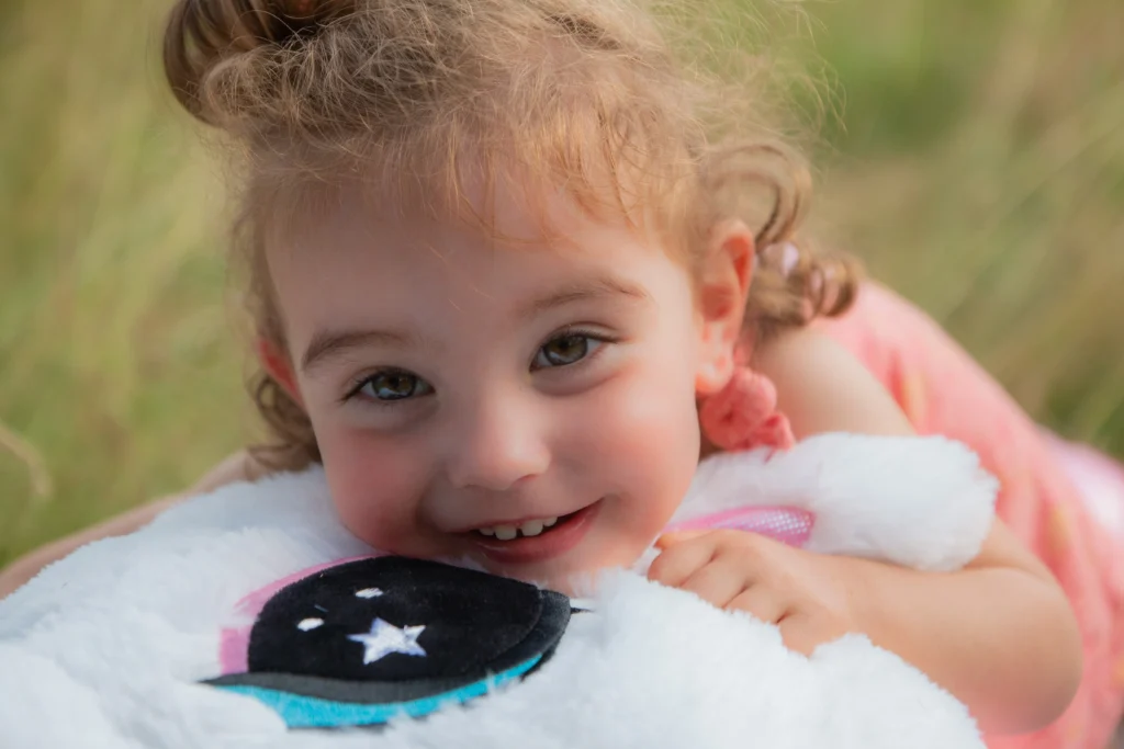 Portrait d’un bébé souriant tenant son doudou lors d’une séance photo à Bagnères-de-Bigorre, réalisée par LS Productions photographe naissance et bébé