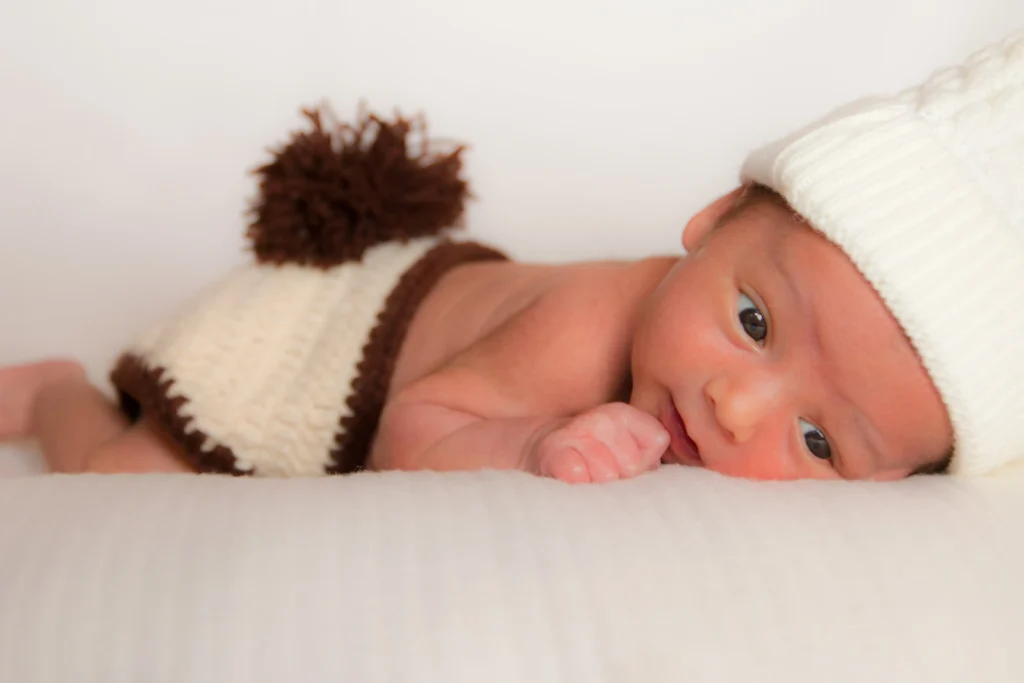Photo de naissance d’un bébé allongé portant un bonnet en laine, réalisée à Bordères-sur-Echez par LS Productions photographe naissance