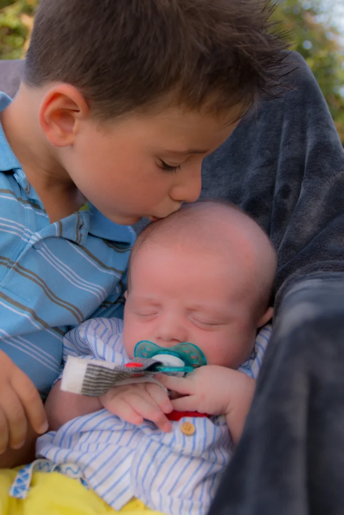 Photo tendre d’un grand frère embrassant son bébé endormi à Tostat, prise par LS Productions photographe naissance