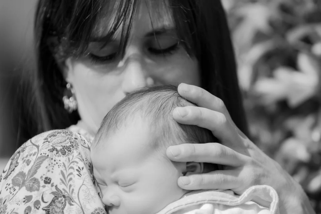 Photo en noir et blanc d’une maman embrassant tendrement son bébé à Lourdes, prise par LS Productions photographe naissance